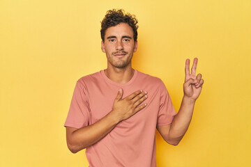 Young Latino man posing on yellow background taking an oath, putting hand on chest.