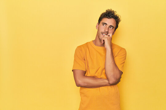 Young Latino man posing on yellow background relaxed thinking about something looking at a copy space.