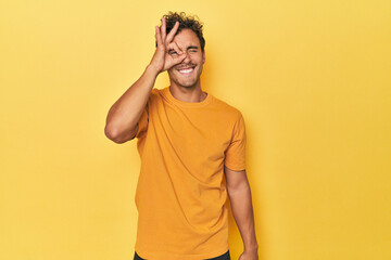 Young Latino man posing on yellow background excited keeping ok gesture on eye.