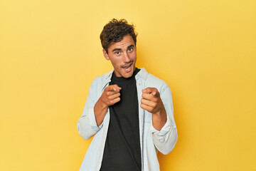 Young Latino man posing on yellow background pointing to front with fingers.