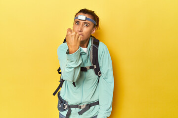 Mountain gear and frontal light on yellow showing fist to camera, aggressive facial expression.