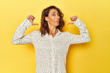 Middle-aged woman on a yellow backdrop feels proud and self confident, example to follow.