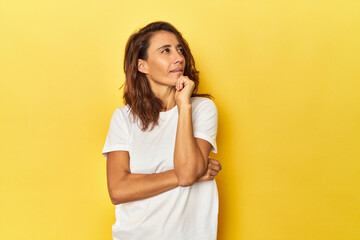 Middle-aged woman on a yellow backdrop thinking and looking up, being reflective, contemplating, having a fantasy.