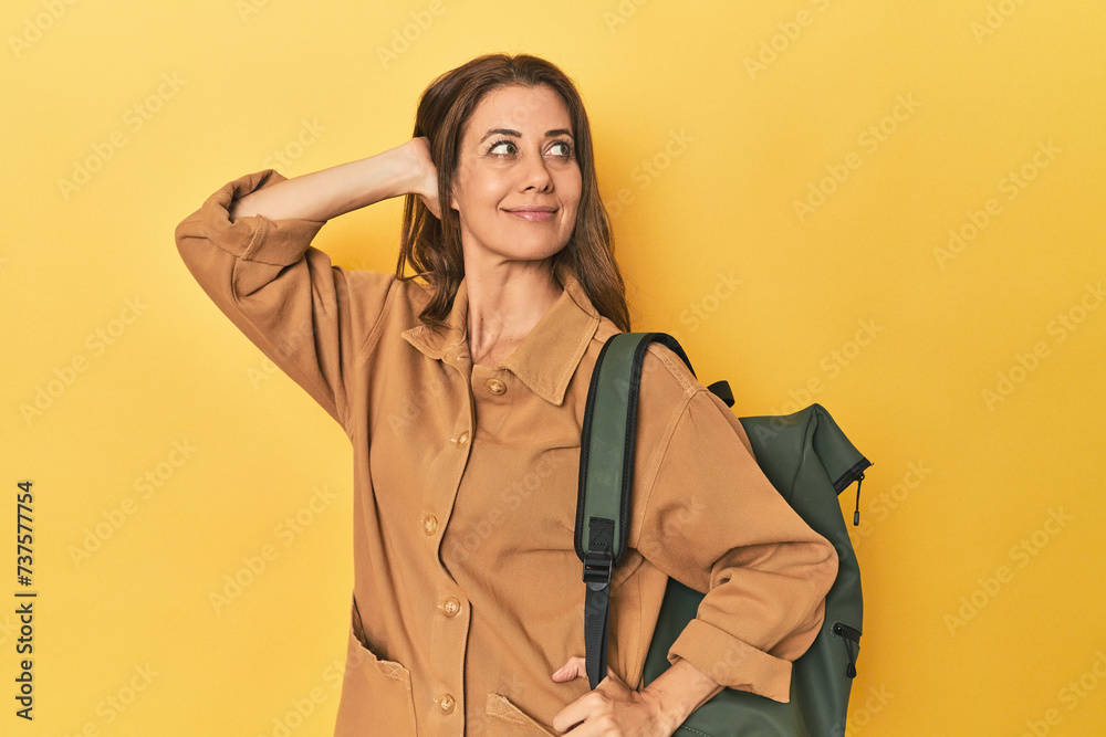 Wall mural Middle aged woman prepped for hiking, yellow studio shot touching back of head, thinking and making a choice.