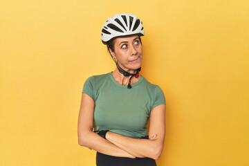 Cyclist middle aged woman with helmet and gloves posed confused, feels doubtful and unsure.
