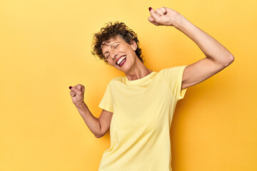 Mid-aged caucasian woman on vibrant yellow celebrating a special day, jumps and raise arms with...