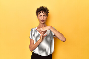 Mid-aged caucasian woman on vibrant yellow showing a timeout gesture.