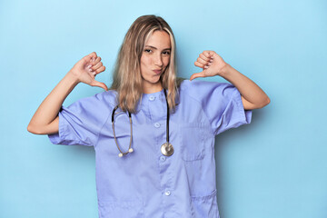 Young caucasian nurse in blue studio feels proud and self confident, example to follow.