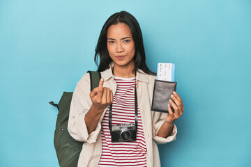 Filipina with camera, tickets, backpack on blue pointing with finger at you as if inviting come...