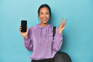Filipina ready for gym with phone on blue showing number two with fingers.