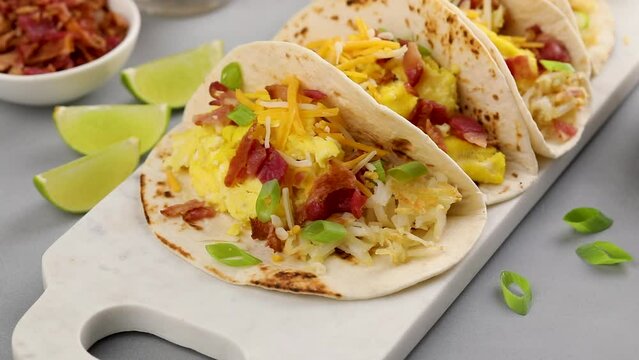 Breakfast tacos with scrambled eggs, bacon and hash browns garnished with green onion, camera slides
