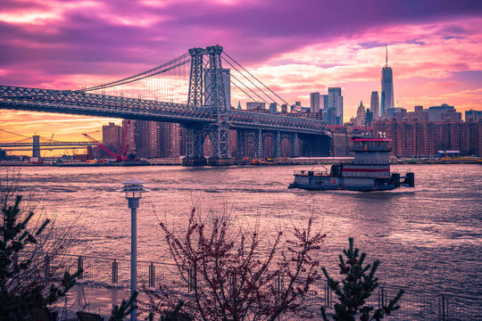 Lower Manhattan Sunset Skyline, Dramatic Saturated Vibrant Purple Clouds, Williamsburg Bridge, Brooklyn Bridge, and Cruising Ferry on the East River in Brooklyn, New York, USA