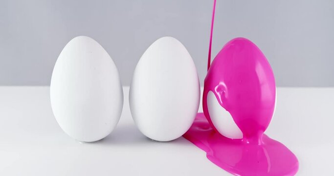 Pouring pink, purple, and blue paint colors over three blank white Easter Eggs. Creative Easter egg decorating.