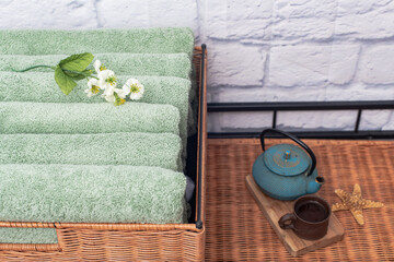 Stacks of bath towels and a kettle of tea on a wicker bedside table in the bathroom.