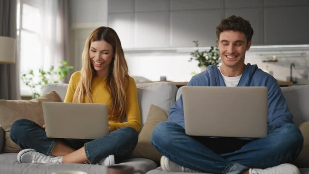Cheerful sweethearts browsing laptops at couch closeup. Couple working computers