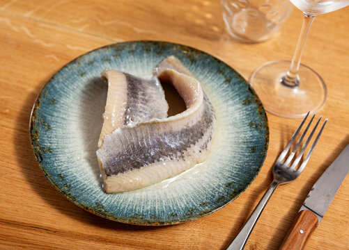 There is of salted herring appetite sild fillet seasoned on white ceramic plate. Traditional Russian snack