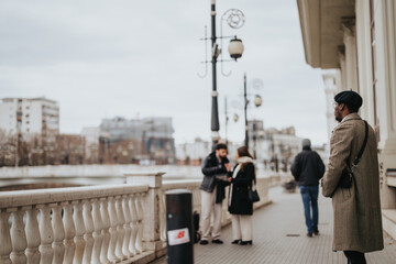 A dapper businessman in a chic overcoat and hat stands absorbed in a phone conversation on an urban sidewalk, with passersby in the background.