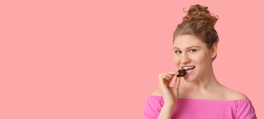 Happy young woman eating chocolate on pink background with space for text