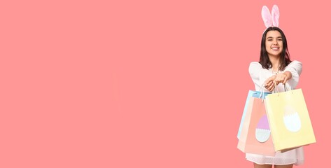 Beautiful young woman with bunny ears and shopping bags on pink background with space for text. Easter sale