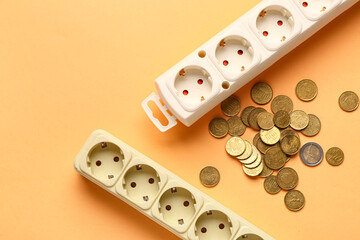 Power sockets with coins on orange background. Electricity bill concept