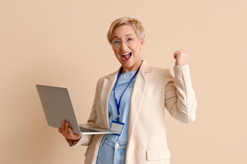 Happy mature female programmer with laptop on beige background