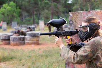 Fototapeta premium Portrait of girl paintball player in mask who is aiming in opponents on paintball field