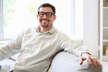 Handsome man in stylish eyeglasses sitting on sofa at home