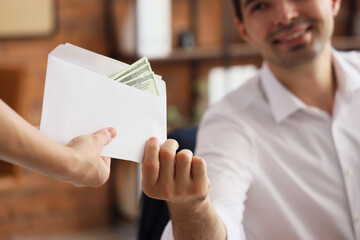 Young businessman taking envelope with money in office, closeup