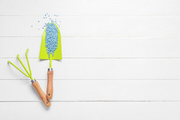 Gardening shovel with blue granular fertilizer and rake on white wooden background