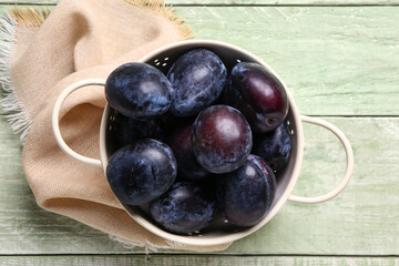 Colander with ripe plums on green wooden background