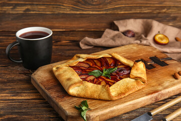 Board of delicious plum galette with mint on wooden background