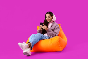 Young woman in jacket using mobile phone on purple background