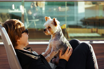 Happy woman with a little Yorkshire terrier dog in the hands relaxing outdoors on resort terrace....
