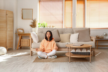 Young Asian woman in stylish hoodie meditating at home