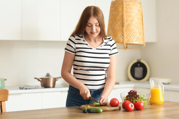 Obraz na płótnie Canvas Young pregnant woman cutting cucumber in kitchen