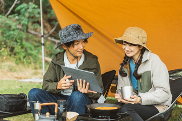 秋冬のキャンプ場でタブレットPCを見ながらキャンプをする男女のキャンパー（Wi-Fi・電源サイト）
