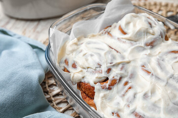 Baking dish of tasty cinnamon rolls with cream on white wooden background