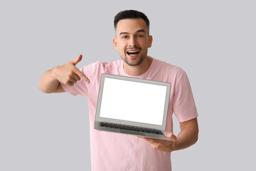 Happy young man pointing at laptop on light background