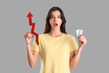 Shocked young woman with pills and arrow on light background. Price rise concept