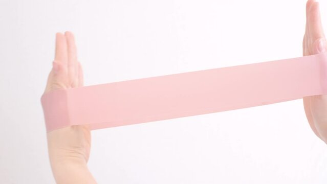 Female hands stretching a pink fitness elastic band on white background close-up.