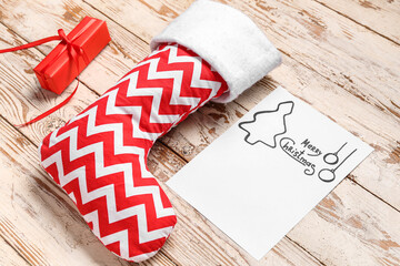 Christmas sock with greeting card and gift box on white wooden background
