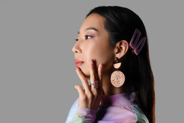 Young Asian woman with beautiful rings and earrings on grey background