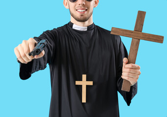 Young priest with gun and cross on blue background, closeup