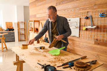 Mature carpenter sweeping filings from table in shop