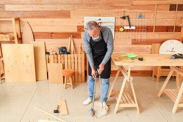 Mature carpenter sweeping filings on floor in workshop