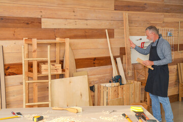 Mature carpenter with wooden planks in workshop