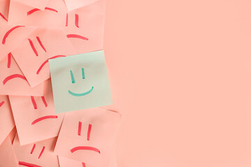 One paper sheet with drawn happy face among sheets with sad ones on pink background. Concept of...