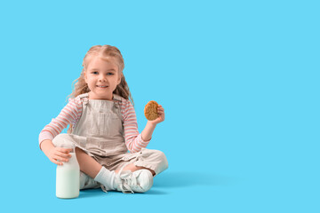 Cute little girl with bottle of milk and cookie sitting on blue background