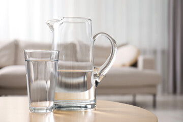 Jug and glass with clear water on table indoors, closeup. Space for text