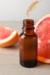 Dripping grapefruit essential oil from pipette into bottle and fresh fruit on light wooden table, closeup